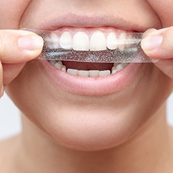 a person putting a whitening strip over their teeth