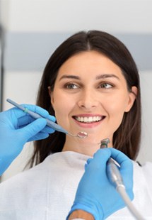 Woman with long brown hair smiling at dentist wearing blue gloves before starting procedure