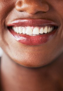 Nose-to-neck view of woman with mauve lips and hoop earrings smiling