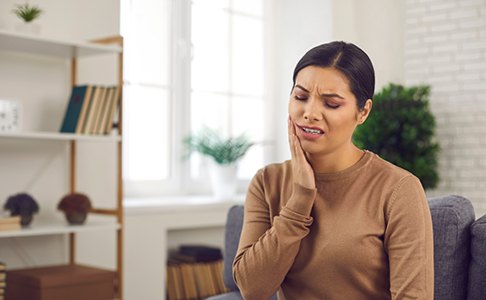 Woman experiencing toothache while sitting on couch